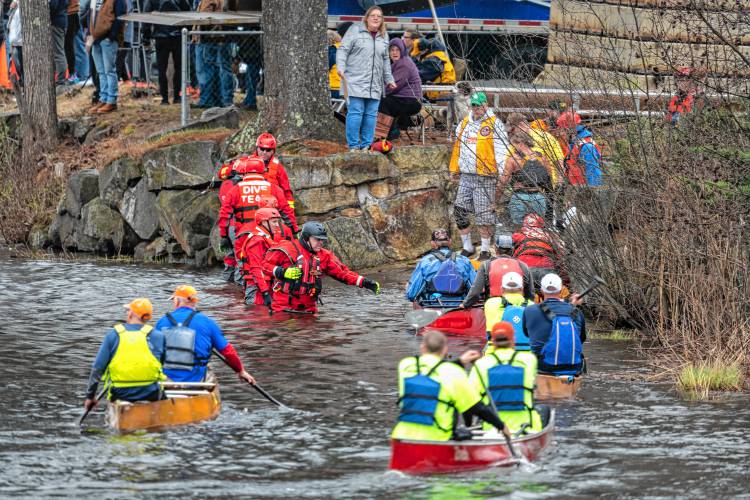 Firefighters and dive teams help canoeists get out of the water after crossing the finish line.
