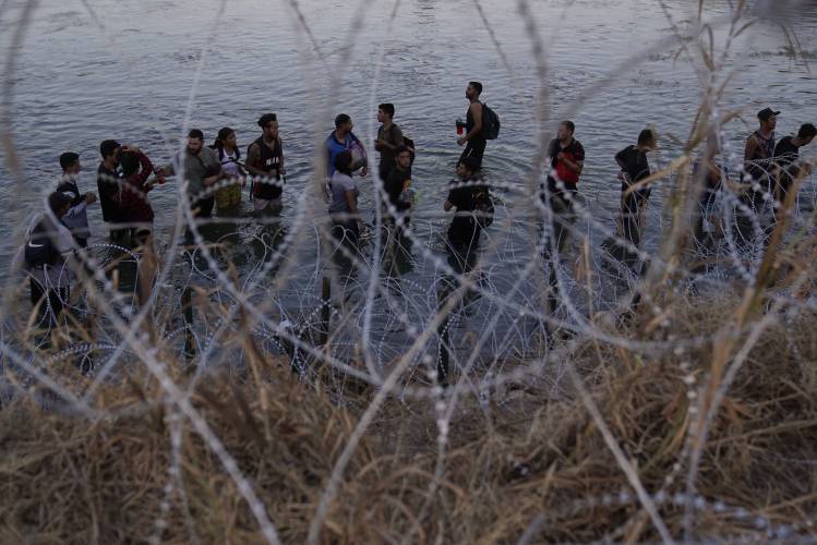 Migrants wait to climb over concertina wire after they crossed the Rio Grande and entered the U.S. from Mexico, Sept. 23, 2023, in Eagle Pass, Texas.