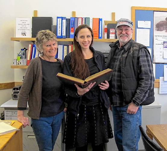 Wendell Town Clerk Anna Wetherby (center) examines a 500-page volume that was recently returned to the town by the Wendell Historical Society. The volume contains town clerk's records for the period 1953-1969. Joining Wetherby are historical society board members Pamela Richardson and Edward Hines.