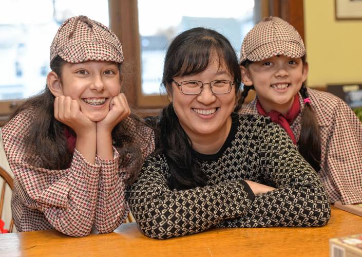 Emma Barrett, 11, mother Cynthia Liu Barrett, and sister Belley Barrett, 8, of Orange, pose in Wheeler Memorial Library, where the sisters will read from their book, “Sister Detectives,” at noon on Saturday.